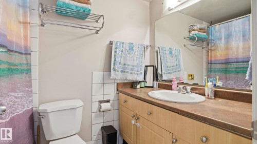 Bathroom featuring a single vanity with an integrated sink, a large wall-mounted mirror, and overhead lighting - 105 5125 Riverbend Road, Edmonton, AB - Indoor Photo Showing Bathroom