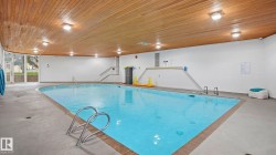 Indoor swimming pool featuring a wood-finish ceiling with recessed lighting, white wall finishes, and a concrete pool deck - 