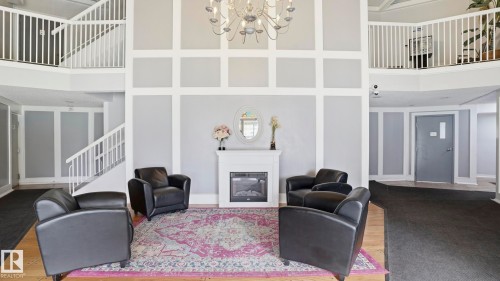 Two-story foyer featuring a central fireplace with white mantel, a chandelier, and a decorative wall paneling system - 105 5125 Riverbend Road, Edmonton, AB - Indoor With Fireplace