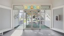 Entrance vestibule featuring a stained glass transom, full-lite glass double doors, a glass sidelight, and a gray carpeted floor - 105 5125 Riverbend Road, Edmonton, AB  - Indoor Photo Showing Other Room 
