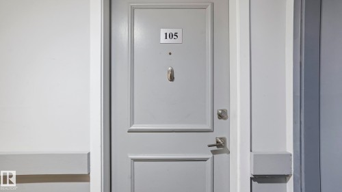 Gray paneled entry door with polished nickel hardware and door knocker - 105 5125 Riverbend Road, Edmonton, AB - Indoor Photo Showing Other Room