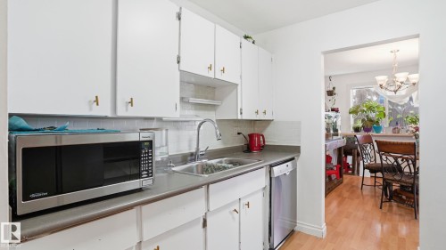 Kitchen featuring white cabinetry with gold-toned hardware, gray countertops, and a white subway tile backsplash - 105 5125 Riverbend Road, Edmonton, AB - Indoor Photo Showing Kitchen With Double Sink