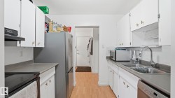 Galley kitchen featuring white cabinetry with brass-tone hardware, grey countertops, and wood-finish flooring - 