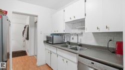 Kitchen featuring white cabinetry with gold-tone hardware, a stainless steel double sink with a gooseneck faucet, gray countertops, and a gray subway tile backsplash - 