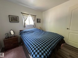 Light-filled bedroom featuring a window with patterned curtains, neutral wall tones, and wood-finish flooring - 