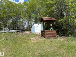 Wood-clad well structure with a shingled roof, accompanied by a metal storage shed and a wooden deck - 