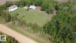 Expansive grounds featuring two distinct structures, a gravel road frontage, and abundant mature trees surrounding the property - 