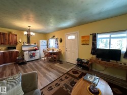 Open-concept living area with wood-finish flooring, a white front door featuring a decorative glass insert, and a kitchen area with natural wood cabinetry and a classic-style range - 