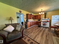Open-concept kitchen featuring wood-finish flooring, rustic wood cabinetry, a classic white range, and a white refrigerator - 