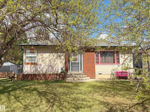 Single-story residence featuring a stucco and brick exterior, a dark shingled roof, and a front yard with mature trees - 5510 Railway Avenue, Glendon, AB - Outdoor