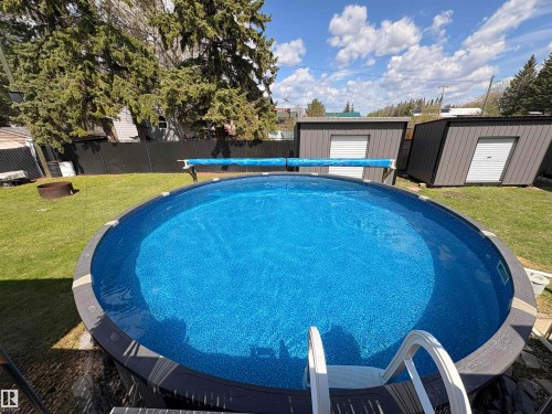 Expansive backyard featuring an above-ground pool, green lawn, mature trees, and two storage sheds with roll-up doors - 5510 Railway Avenue, Glendon, AB - Outdoor With Above Ground Pool With Backyard