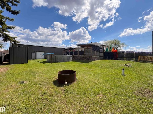 Expansive green lawn featuring an above-ground pool, a metal utility building, a large metal-sided outbuilding with a white roll-up door, and a wooden deck with a privacy fence - 5510 Railway Avenue, Glendon, AB - Outdoor