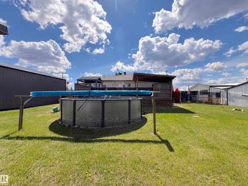Expansive backyard featuring an above-ground pool, covered deck area, and a large metal-clad outbuilding - 5510 Railway Avenue, Glendon, AB - Outdoor With Above Ground Pool