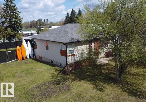 Spacious lawn with established perimeter fencing, mature shade trees, and a foundation-level window - 5510 Railway Avenue, Glendon, AB - Outdoor