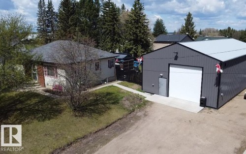 Property featuring a large, modern grey metal-sided outbuilding with a white roll-up door and a side entry door - 5510 Railway Avenue, Glendon, AB - Outdoor
