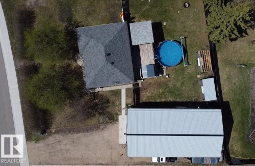 Expansive property featuring a main residence with a dark shingle roof, a detached structure with a light-colored metal roof, and an above-ground pool - 5510 Railway Avenue, Glendon, AB - Outdoor