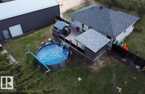 Expansive backyard featuring an above-ground swimming pool, a wood deck, and a screened patio with shingled roof - 5510 Railway Avenue, Glendon, AB - Outdoor With Above Ground Pool With Deck Patio Veranda