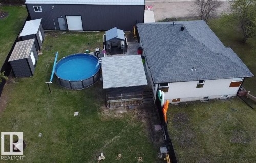 Rear exterior featuring an above-ground pool, a spacious deck with covered pergola, a large detached metal-sided building, and two additional storage sheds - 5510 Railway Avenue, Glendon, AB - Outdoor With Above Ground Pool
