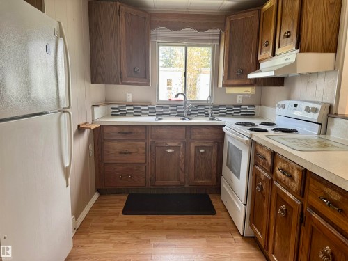 Kitchen featuring wood-finish cabinetry, white countertops, a mosaic tile backsplash, a stainless steel sink, and wood-finish flooring - #46 4204 47 St, Wetaskiwin, AB - Indoor Photo Showing Kitchen