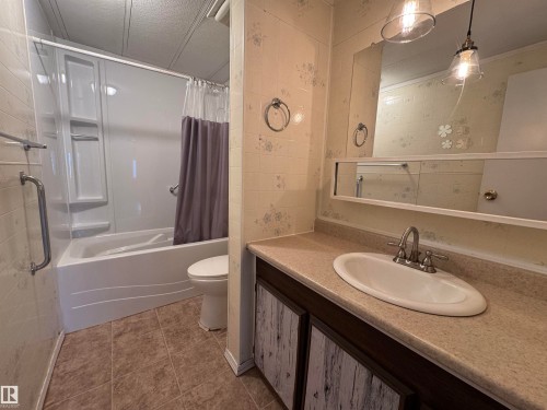 Bathroom featuring a white bathtub with an integrated shower, a white toilet, and a vanity with a light-toned countertop and an oval sink - #46 4204 47 St, Wetaskiwin, AB - Indoor Photo Showing Bathroom