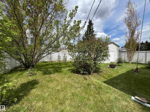 Expansive backyard featuring a green lawn, mature trees, a white lattice fence, and a white storage shed - #46 4204 47 St, Wetaskiwin, AB - Outdoor