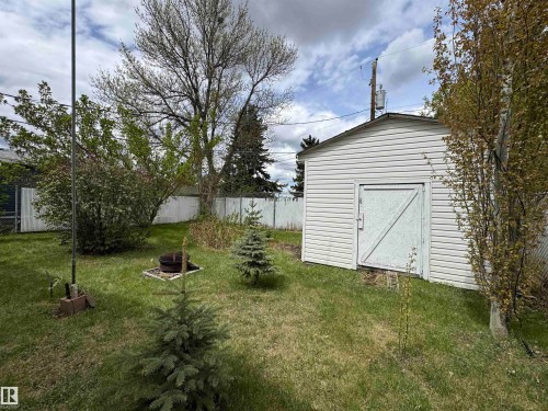 Rear yard featuring a white vinyl-sided storage shed with a single door, established trees, and a metal fire pit - #46 4204 47 St, Wetaskiwin, AB - Outdoor