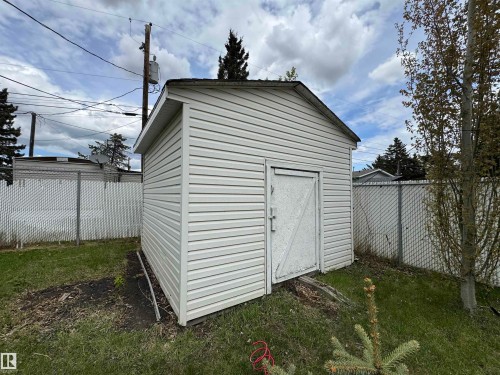 Detached storage shed with white siding, a sloped roof, and a single wooden access door - #46 4204 47 St, Wetaskiwin, AB - Outdoor