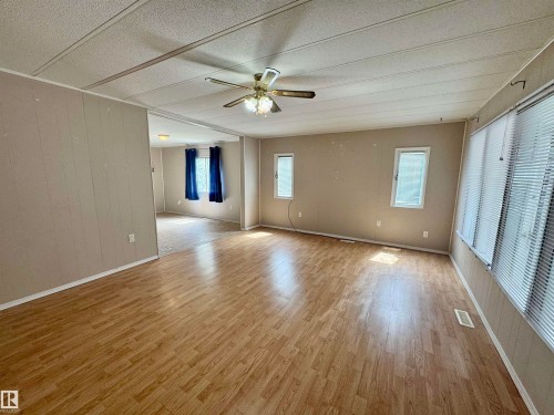 Spacious living area featuring wood-finish flooring, a ceiling fan, multiple windows with blinds, and neutral-toned wall paneling - #46 4204 47 St, Wetaskiwin, AB - Indoor Photo Showing Other Room