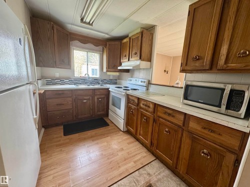 Kitchen featuring wood cabinetry, white countertops, a mosaic tile backsplash, a double basin sink, and wood-finish flooring - #46 4204 47 St, Wetaskiwin, AB - Indoor Photo Showing Kitchen