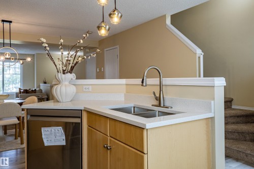 Kitchen island featuring a stainless steel double basin sink with a brushed nickel faucet, light wood cabinetry, and a light-colored countertop - 41 8304 11 Avenue, Edmonton, AB - Indoor Photo Showing Kitchen With Double Sink