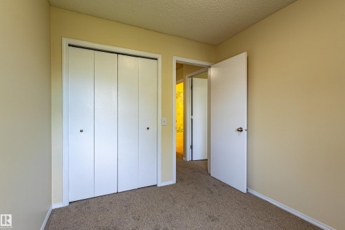Neutral-toned carpeted room featuring a four-panel bi-fold closet with white doors and baseboards - 41 8304 11 Avenue, Edmonton, AB - Indoor