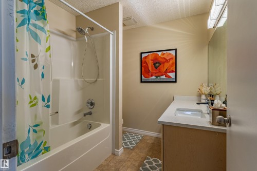 Full bathroom featuring a white tub and shower combination with chrome fixtures, a single vanity with a white countertop and integrated sink, a large wall-mounted mirror, and wood-finish flooring - 41 8304 11 Avenue, Edmonton, AB - Indoor Photo Showing Bathroom