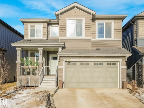 Two-story home with a prominent front entrance, featuring a covered porch with stone-clad pillars and a white railing - 8641 Mayday Wynd, Edmonton, AB - Outdoor