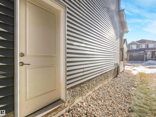 Cream-paneled exterior door with brushed nickel hardware, set against two-tone siding - 8641 Mayday Wynd, Edmonton, AB - Outdoor With Exterior