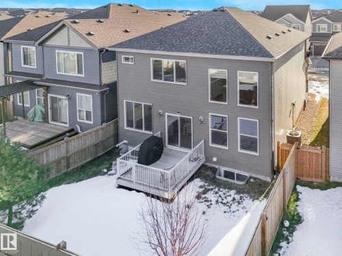 Rear exterior featuring a grey siding facade, multiple windows, a ground-level deck with white railing, and a fenced backyard - 8641 Mayday Wynd, Edmonton, AB - Outdoor