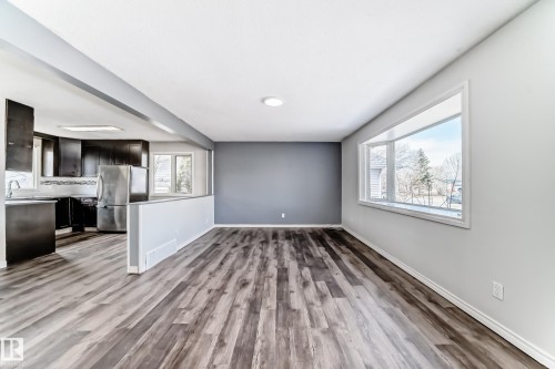 Spacious living area featuring wood-finish flooring, a broad picture window, a flush-mount ceiling light, and a partial wall separating it from the kitchen - 8615 42A Avenue, Edmonton, AB - Indoor