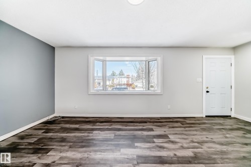 Bright interior space featuring a multi-pane bay window, dark wood-finish flooring, a contemporary accent wall, and a paneled entry door - 8615 42A Avenue, Edmonton, AB - Indoor Photo Showing Other Room