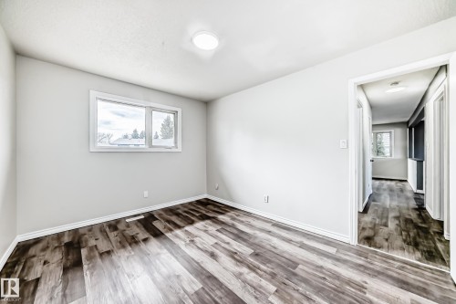 Room featuring expansive wood-finish flooring, light grey painted walls, a large window with white trim, and a flush-mount ceiling light - 8615 42A Avenue, Edmonton, AB - Indoor Photo Showing Other Room