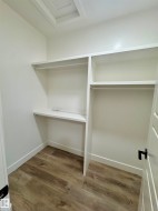 Walk-in closet featuring wood-finish flooring, white walls, and built-in shelving with hanging rods - 