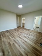 Spacious room featuring wood-finish flooring, light-toned walls, and a ceiling-mounted light fixture - 