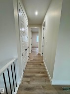 Hallway with wood-finish flooring, white paneled doors, and contemporary black hardware - 