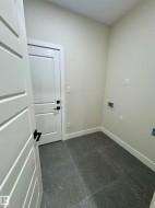 Utility room featuring dark gray speckled tile flooring, light neutral wall paint, and white trim - 
