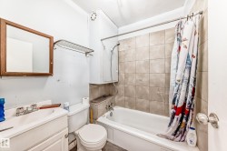 Bathroom with a white vanity sink, a toilet, and a bathtub featuring beige wall tiling - 