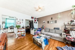 Spacious living area featuring wood-finish flooring, a neutral ceiling with a ceiling fan, and a light brown accent wall - 