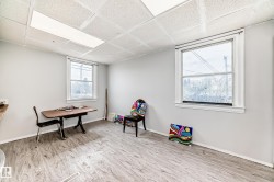 Spacious room featuring wood-finish flooring, light gray walls, and a drop ceiling with recessed lighting - 