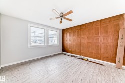 Room featuring a wood-finish accent wall, light wood-finish flooring, two large windows with white trim, a ceiling fan, and light gray wall paint - 