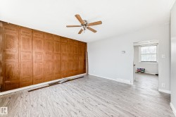 Room featuring a wood-panel accent wall, light-toned wood-finish flooring, and a ceiling fan - 