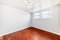 Room featuring wood-finish flooring, two large windows, a white ceiling fan with light fixture, and white baseboards - 