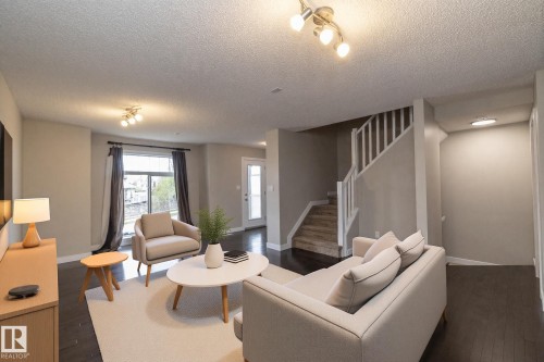 Spacious living area featuring dark wood-finish flooring, a contemporary staircase with white balusters, light gray wall paint, and recessed lighting fixtures - 117 Callaghan Drive Sw, Edmonton, AB - Indoor Photo Showing Living Room
