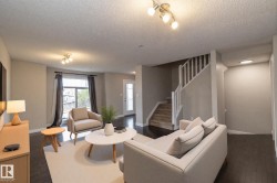 Spacious living area featuring dark wood-finish flooring, a contemporary staircase with white balusters, light gray wall paint, and recessed lighting fixtures - 